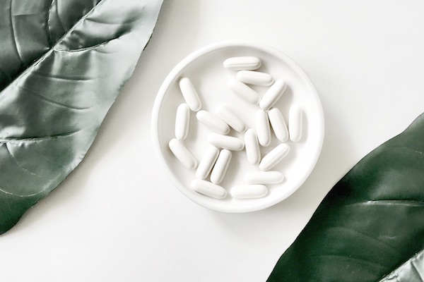 Pills in bowl next to two large leaves